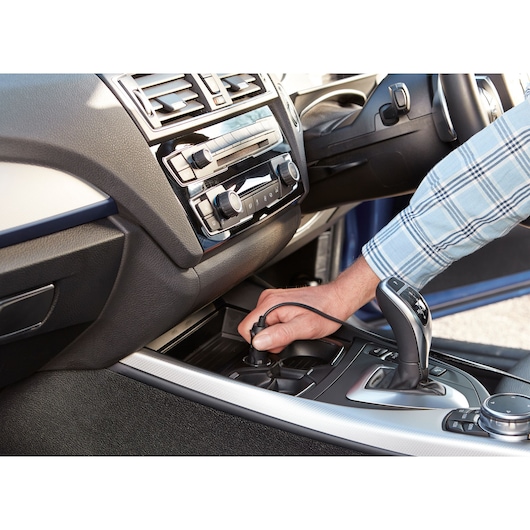 BLACK+DECKER ASI400 car air compressor plugged into vehicle socket, hand connecting power cable in car interior.