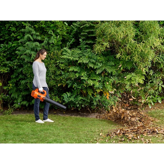 BLACKDECKER BCBL200B cordless leaf blower in use blowing leaves on grass in a garden.