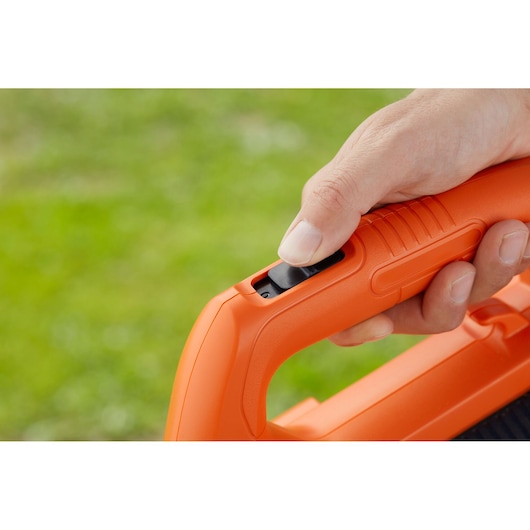 Close-up photo of a hand pressing the power button on an orange BLACKDECKER BCBL200B blower handle.
