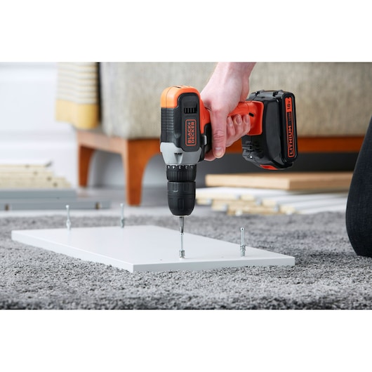 BLACK+DECKER BCD001C2 cordless drill used to assemble white furniture panel on gray carpet, close-up.