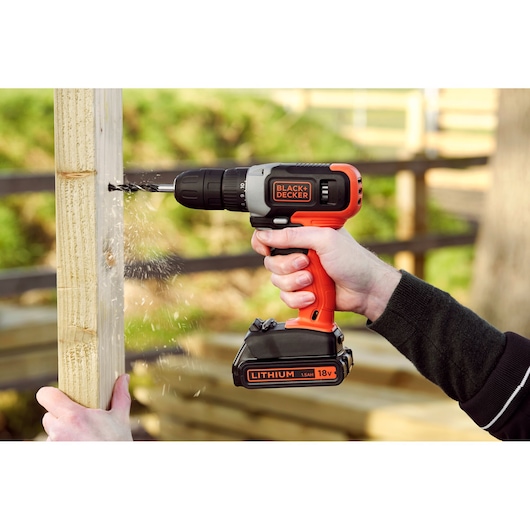 Photo of BLACK+DECKER 18V cordless drill BCD001C2 in use drilling into wood outdoors.