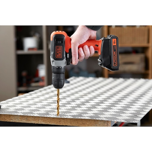BLACKDECKER cordless drill BCD001C2 drilling into metal sheet, side angle, orange and black.