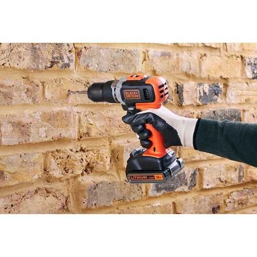 Photo of BLACKDECKER BCD003ME2K cordless drill in use drilling into brick wall, user wearing protective glove.