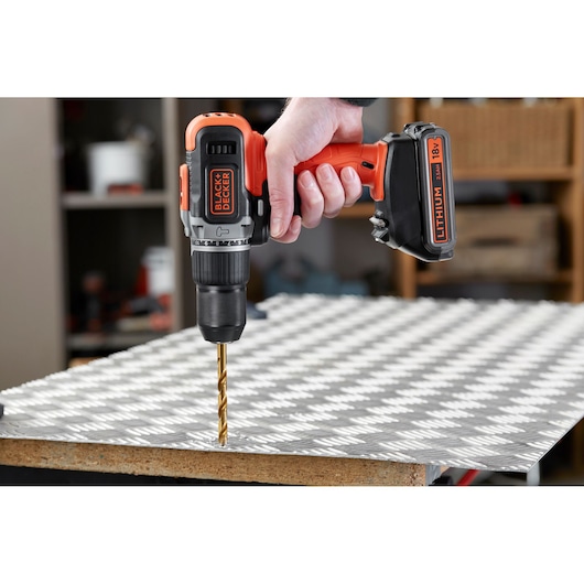 BLACK+DECKER BCD003MEM2K cordless drill with orange and black design used to drill metal sheet, close-up side view.