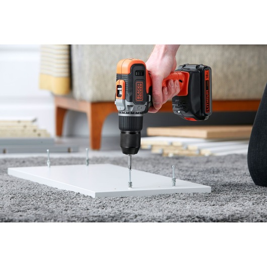 BLACK+DECKER BCD003MEM2K cordless drill driving a screw into a white board on a grey carpet.