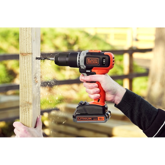 Photo of BLACK+DECKER BCD003MEM2K cordless drill in use, drilling into wood, visible lithium 18V battery.