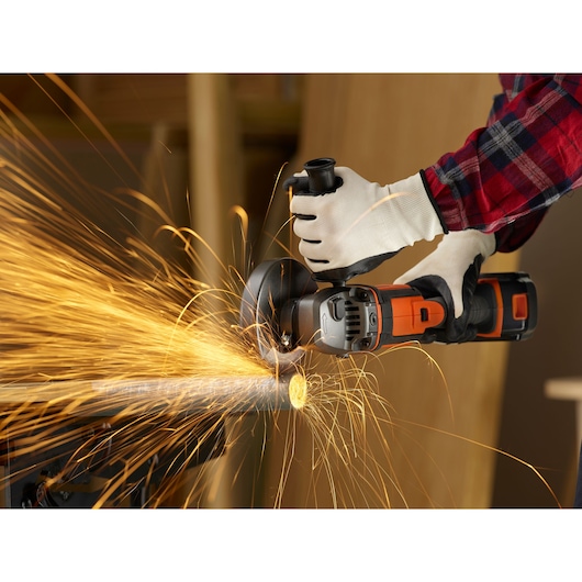 Photo of BLACKDECKER BCG720M1 cordless angle grinder cutting metal pipe, sparks flying, close-up action shot.