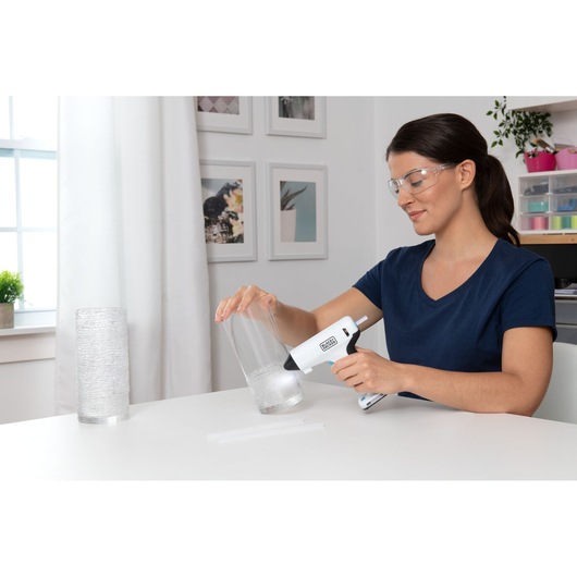 BLACKDECKER BCGL115 glue gun held by person applying glue to clear glass vase in craft workspace.