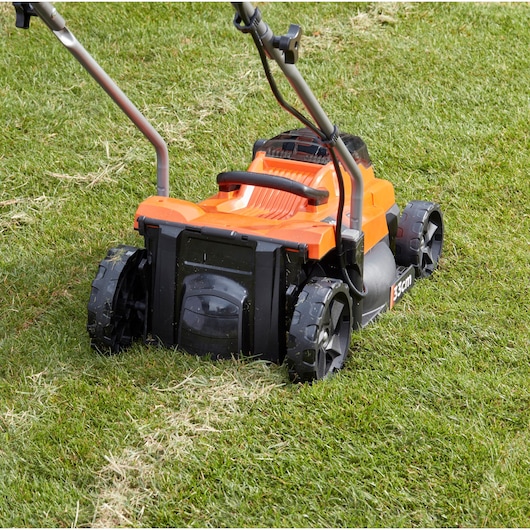 BLACKDECKER BCMW33185L2 cordless lawn mower, orange, rear view on grass, 33cm cutting width.