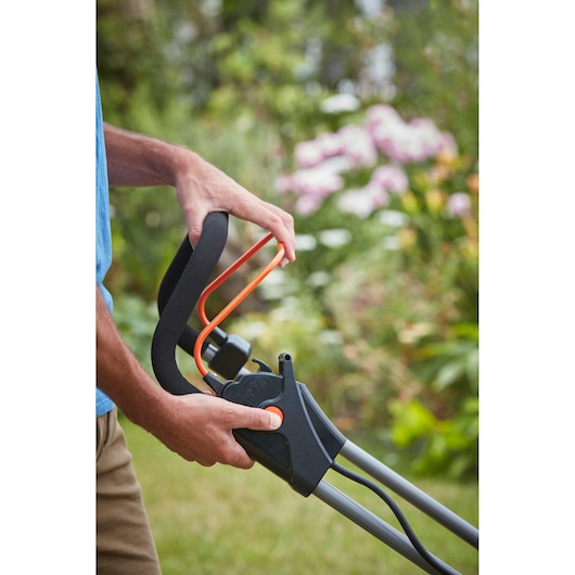 Close-up photo of BLACKDECKER BCMW33185L2 lawn mower handle with user operating the control lever outdoors.