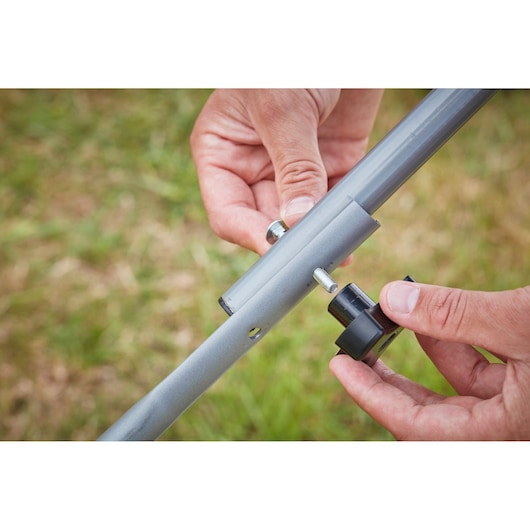 Close-up of hands assembling BLACK+DECKER BCMW3336L1 metal frame with bolt and knob outdoors.