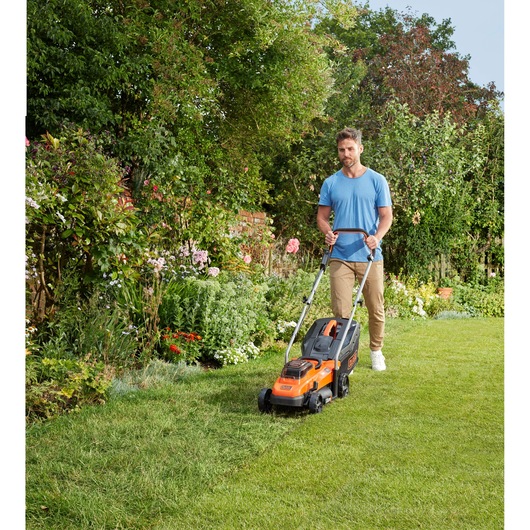 BLACKDECKER BCMW3336L2 lawn mower in use on grass in a garden, user pushing the orange and black mower forward.
