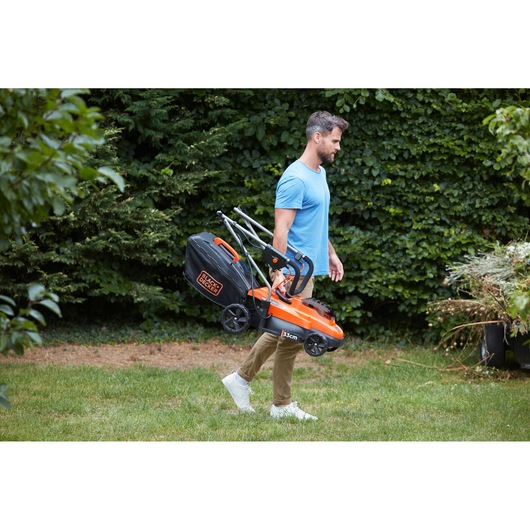 BLACKDECKER BCMW3336L2 lawn mower with folding handle carried outdoors by a person, orange and black design.