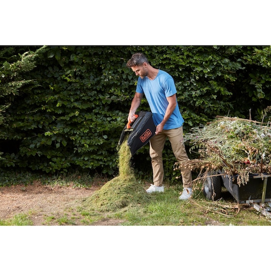 Photo of BLACKDECKER lawn mower grass box BCMW3336L2 being emptied outdoors onto a pile of cut grass.