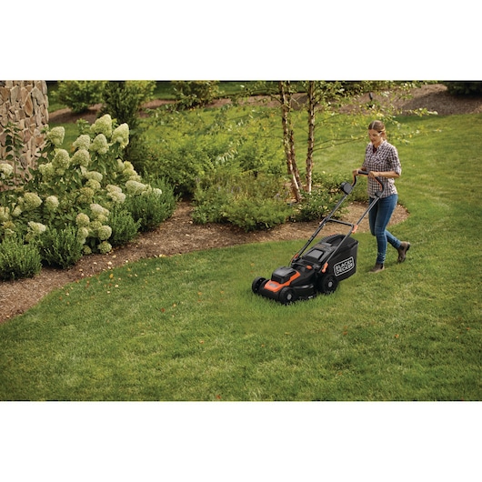 A person mowing the lawn with a BLACK+DECKER electric lawn mower in a green garden.