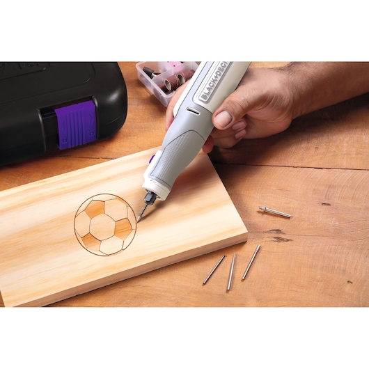 BLACKDECKER BCRT8IPETK rotary tool engraving a soccer ball design on wood, accessories and case visible.