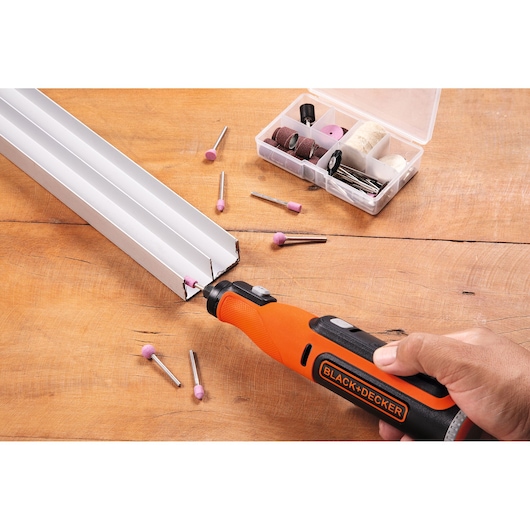 BLACKDECKER BCRT8I cordless rotary tool used on metal, accessory kit and attachments on wood surface.