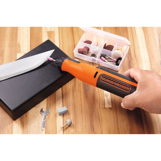 Photo of BLACK+DECKER BCRT8I rotary tool in use with accessory kit, sharpening a knife on wooden surface.