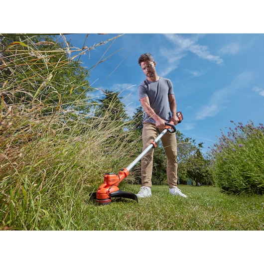 BLACKDECKER BCSTA536B grass trimmer in use outdoors trimming tall grass, orange and silver design.