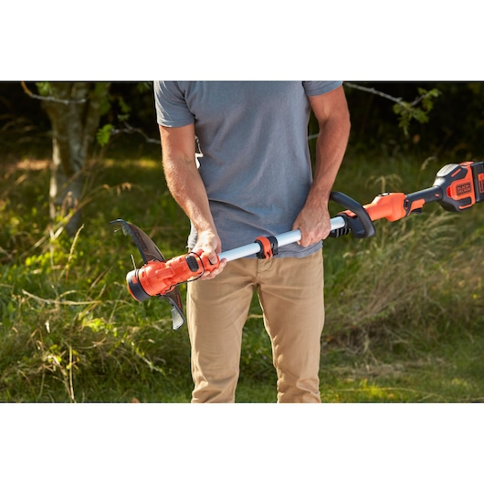 Photo of person holding BLACKDECKER BCSTA536B orange cordless grass trimmer in a garden.