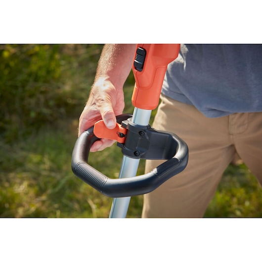 Photo of BLACKDECKER BCSTA536B grass trimmer handle adjustment, close-up of user adjusting black and orange handle outdoors.
