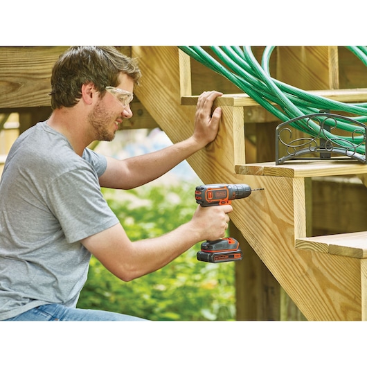 BLACKDECKER BDCDC18 cordless drill used outdoors on wooden stairs, visible orange and black design.