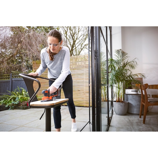 Photo of BLACKDECKER BDCDS18N sander being used on a chair outdoors near a patio door.
