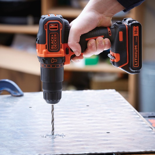 Photo of BLACKDECKER BDCHD18S2KA cordless drill in use, drilling metal surface, close-up view.
