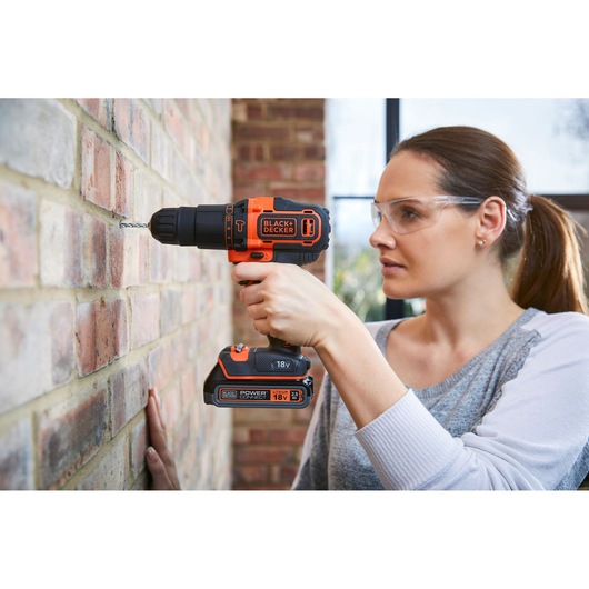 Photo of BLACK+DECKER BDCHD18S2KA cordless drill in use, drilling into a brick wall.