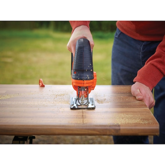 BLACKDECKER BDCJS18N jigsaw cutting wood plank outdoors, close-up of tool and work surface.