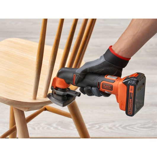 Photo of BLACKDECKER BDCOS18N cordless sander smoothing wooden chair with orange and black design.