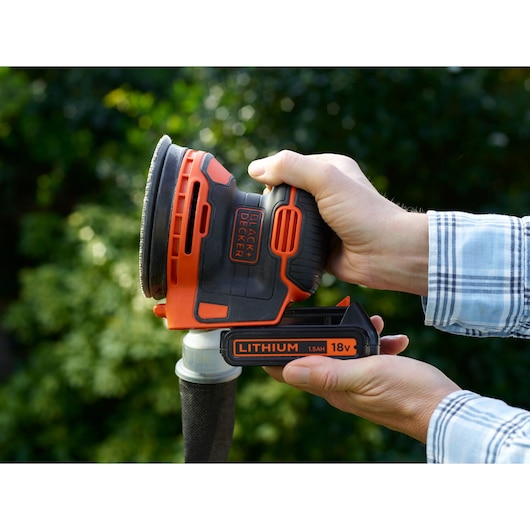 Photo of BLACKDECKER BDCROS18 cordless 18V random orbital sander held in hand outdoors.