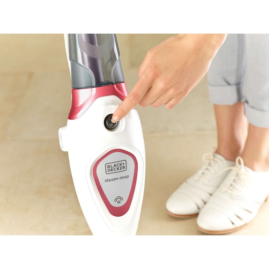 Photo of BLACK+DECKER BDS1616R steam mop being activated on beige floor by a hand, red and white design.