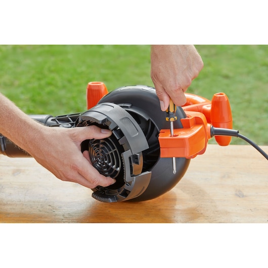 Photo of hands repairing BLACK+DECKER BEBLV260 leaf blower, close-up on motor housing and screwdriver.