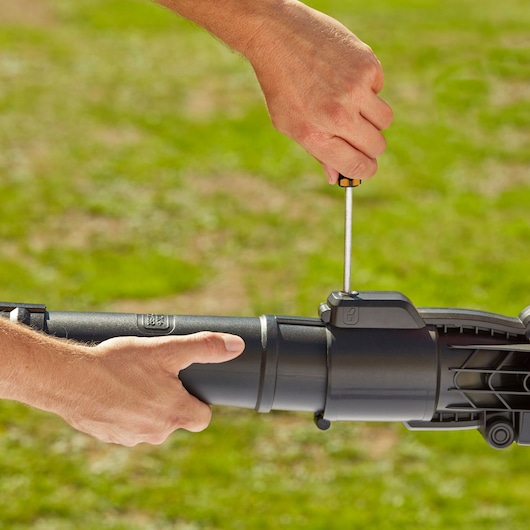 Close-up of hands assembling BLACKDECKER BEBLV290 leaf blower tube outdoors with screwdriver.