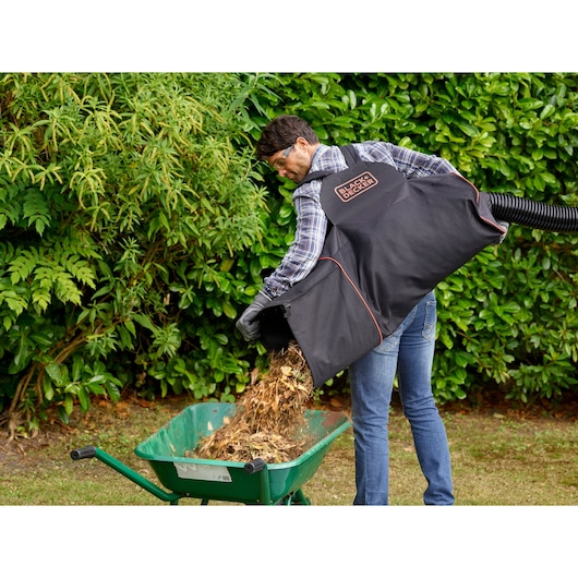 BLACKDECKER BEBLV301 garden vacuum bag emptying mulch into green wheelbarrow outdoors.