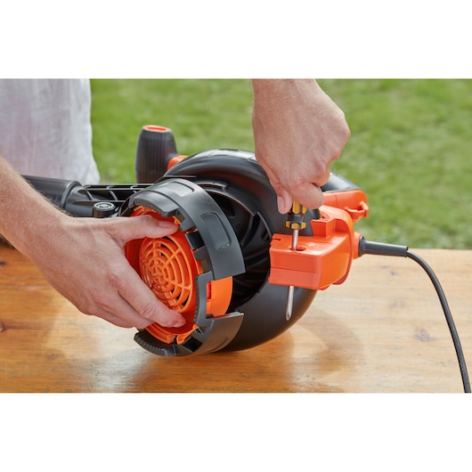 BLACKDECKER BEBLV301 leaf blower close-up, person adjusting orange guard with screwdriver on wooden table.