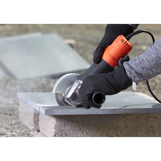 Photo of BLACKDECKER BEG210KDG angle grinder with black and orange body, cutting stone tile, handled by gloved hands.
