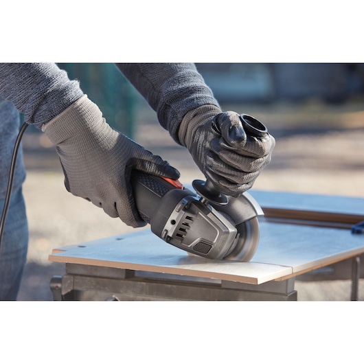 BLACKDECKER BEG210KDG angle grinder used to cut tile outdoors, close-up of gloved hands.