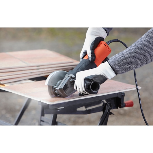 BLACKDECKER BEG210 angle grinder in use cutting tile, user wearing gloves, close-up photography.