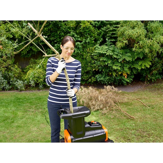 BLACKDECKER BEGAS5800 garden shredder in use outdoors, person feeds tree branch into machine.