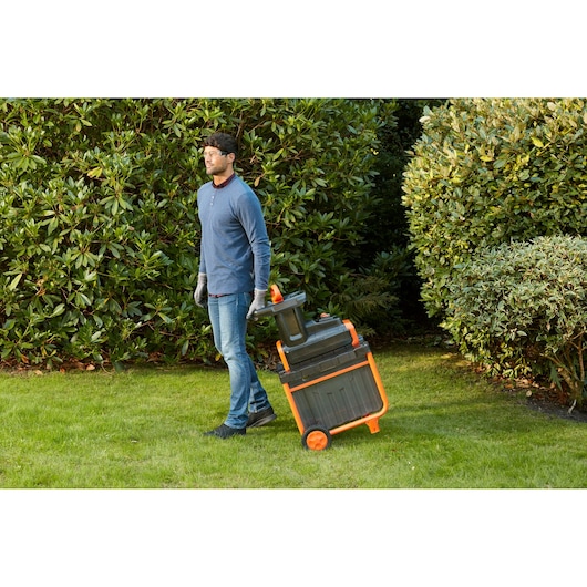 Photo of a person pulling a BLACKDECKER BEGAS5800 garden shredder with orange wheels on grass.