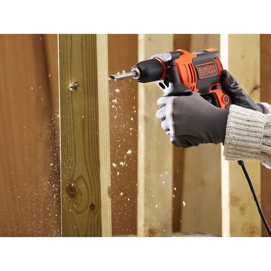 BLACKDECKER BEH550 corded drill in use, drilling through wooden beams with sawdust flying.