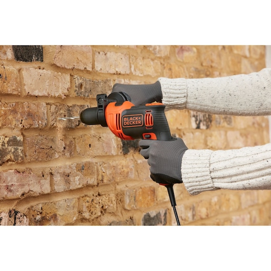 BLACK+DECKER BEH550 corded hammer drill in use drilling into a brick wall, shown in operator hands.