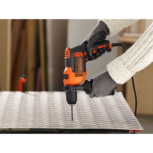 Photo of BLACK+DECKER BEH550 corded drill with side handle in use drilling into metal sheet.