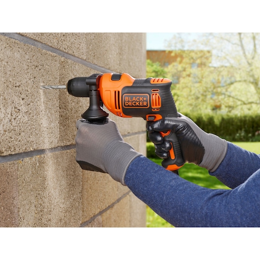BLACKDECKER BEH550 orange and black hammer drill in use drilling into outdoor stone wall.