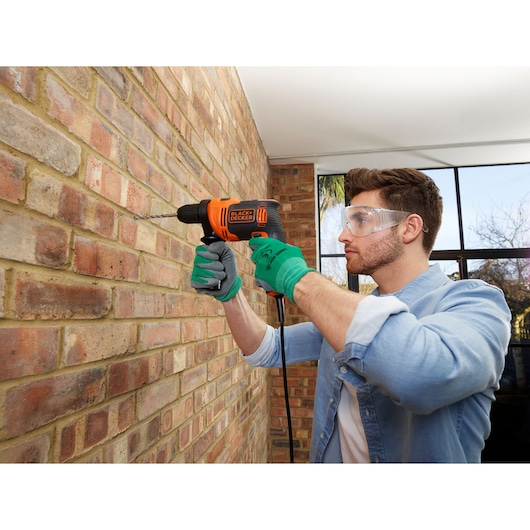 BLACKDECKER BEH710K corded drill used on brick wall, person wearing gloves and denim shirt.