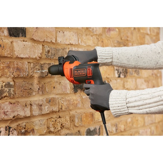 BLACK+DECKER BEH710SA32 hammer drill in use on a brick wall, close-up side view.