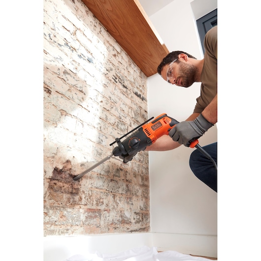 BLACKDECKER BEHS01K rotary hammer drill being used on brick wall, orange and black tool, side angle.