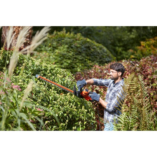 BLACKDECKER BEHTS401 hedge trimmer used outdoors for trimming dense green bushes.